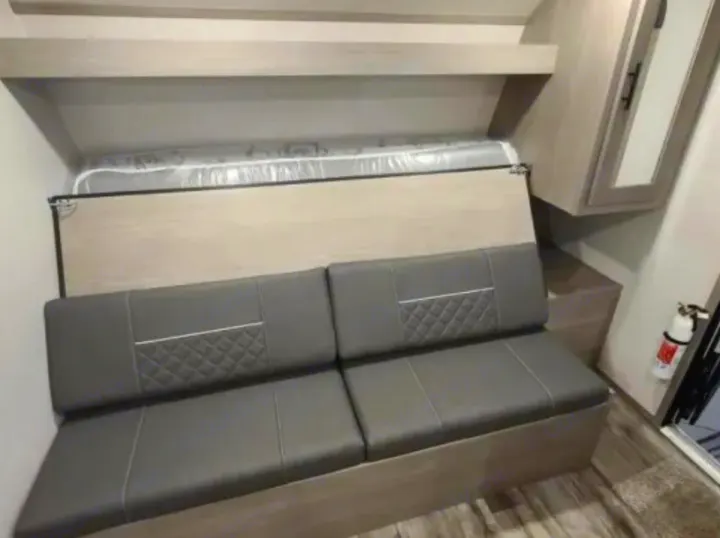 RV rental interior features grey dinette seating below an overhead bunk bed. Compact space with cabinet & fire extinguisher.. Dutchmen Coleman Lantern LT 2021