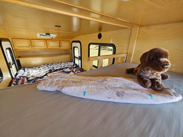 Cozy RV rental interior featuring two comfortable beds, light wood paneling, and a brown stuffed dog.. Escapade Ridge 2018
