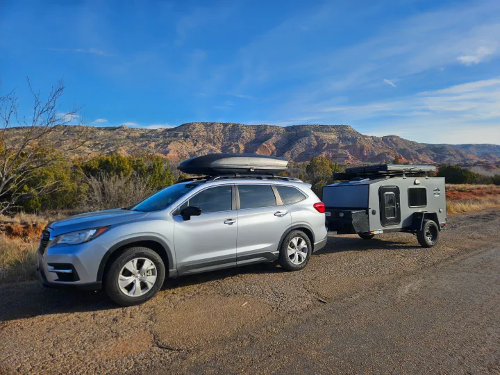 Silver SUV towing a grey teardrop camper with rooftop gear in a mountain landscape, great for an RV rental trip.. Escapade Ridge 2018