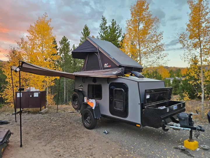 Enjoying fall colors with an RV rental: a modern teardrop camper with a rooftop tent and awning, surrounded by vibrant yellow aspens.. Escapade Ridge 2018