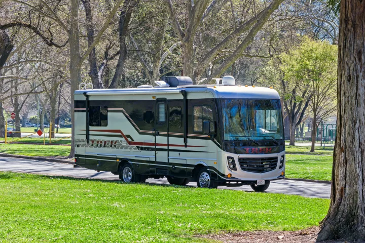 Modern Class A RV rental parked in a sunny park with vibrant green grass and large trees. Ideal for road trips.. Monaco Trek 26HMD 2016