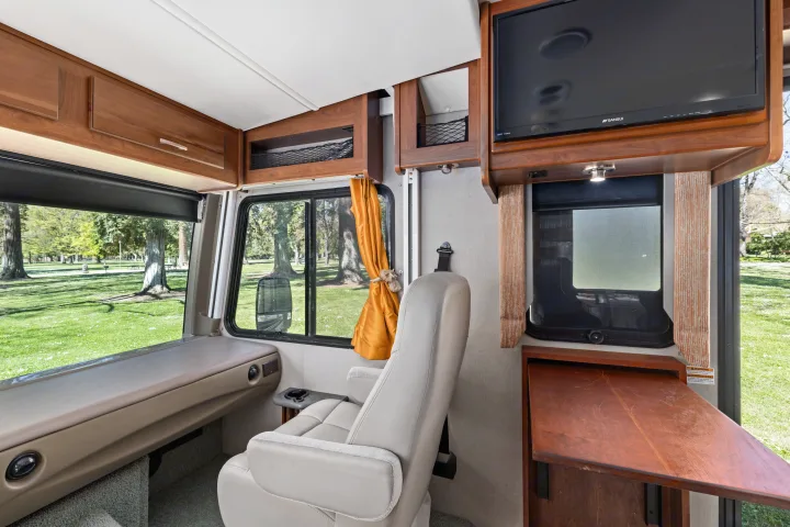 Inside an RV rental: a cozy living area with wooden cabinets, TV, and a beautiful green park view outside.. Monaco Trek 26HMD 2016