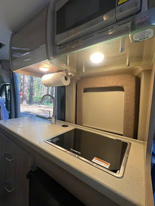 Modern RV rental kitchen with a Dometic cooktop, sink, and microwave. Brightly lit, ready for camping adventures.. Thor Motor Coach Sequence 2022