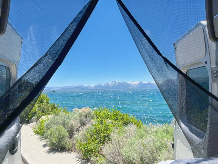 Stunning lake view from an RV rental, framed by screens. Snowy mountains across sparkling water and green plants.. Thor Motor Coach Sequence 2022