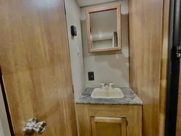 Cozy RV rental bathroom: wood-paneled walls, compact sink, mirrored vanity, and thermostat. Ideal for travel.. Keystone RV Summerland 2017