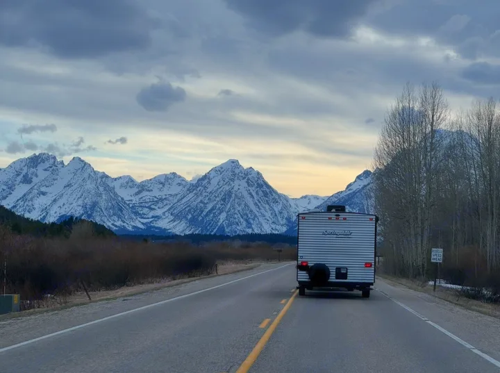 An rv rental travels a scenic road with snow-capped Grand Teton mountains under a cloudy sky.. Keystone RV Summerland 2017