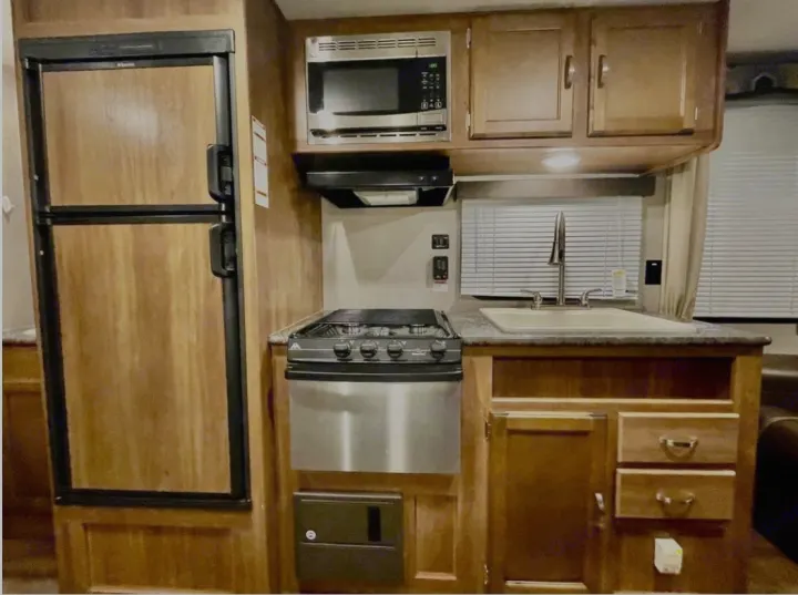 Compact RV rental kitchen featuring a fridge, microwave, stove, and sink. Ready for your adventure meals.. Keystone RV Summerland 2017