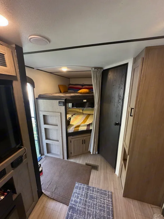 Inside this modern RV rental: comfy bunk beds with privacy curtain, a dark door, and entertainment area. Bright and spacious camper.. Keystone Hideout 2021