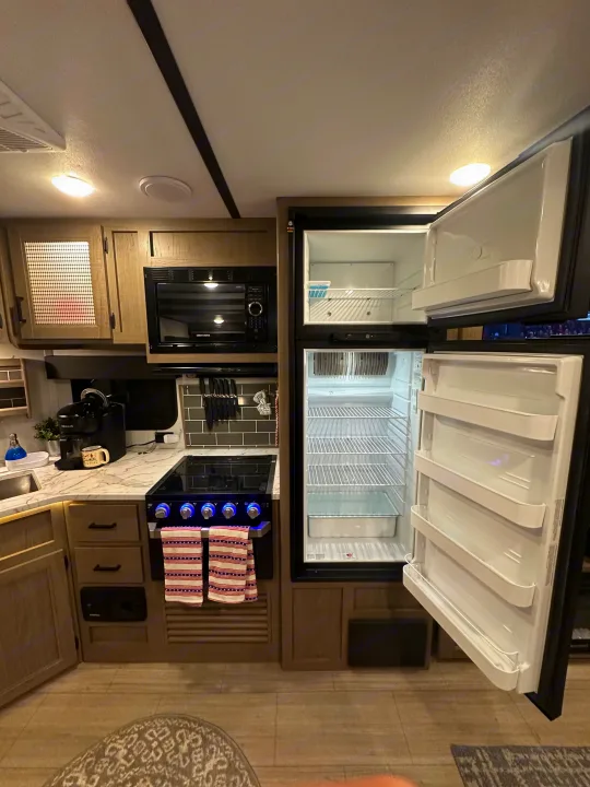 Inside an RV rental: a compact kitchen with an open refrigerator, microwave, stove, and coffee maker area.. Keystone Hideout 2021