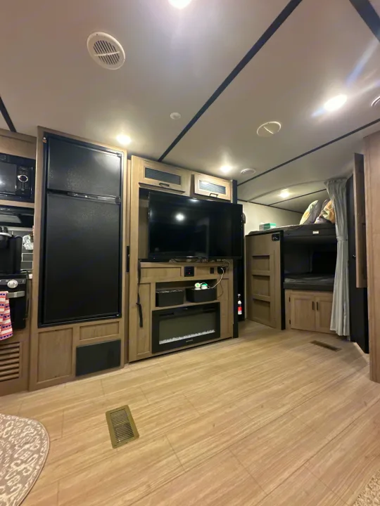 Inside an RV rental: a modern living area with a large TV, electric fireplace, refrigerator, and bunk beds. Perfect for family trips.. Keystone Hideout 2021