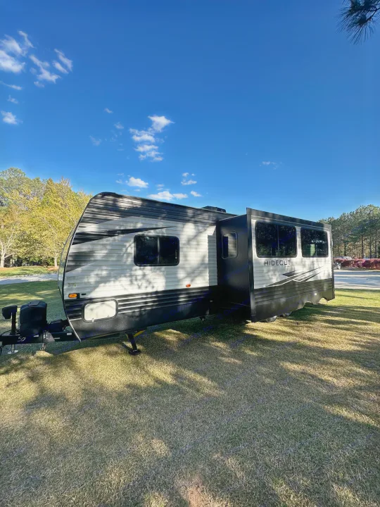 Bright blue sky over an RV rental, a large Keystone Hideout travel trailer, parked on lush grass in sunlight.. Keystone Hideout 2021