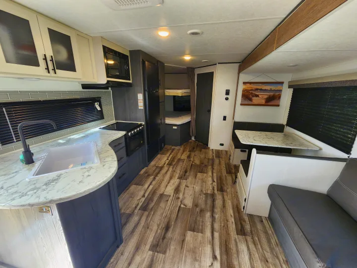 Spacious rv rental interior with kitchenette, dining booth, and bunk beds, featuring modern finishes and wood-look flooring.. Dutchmen Aspen Trail 26BH 2025