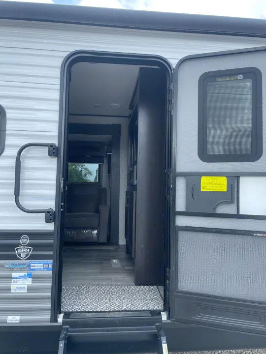 An rv rental's open door shows the interior, revealing sleek flooring, a black recliner, and built-in cabinetry.. Jayco Jay Flight 2022