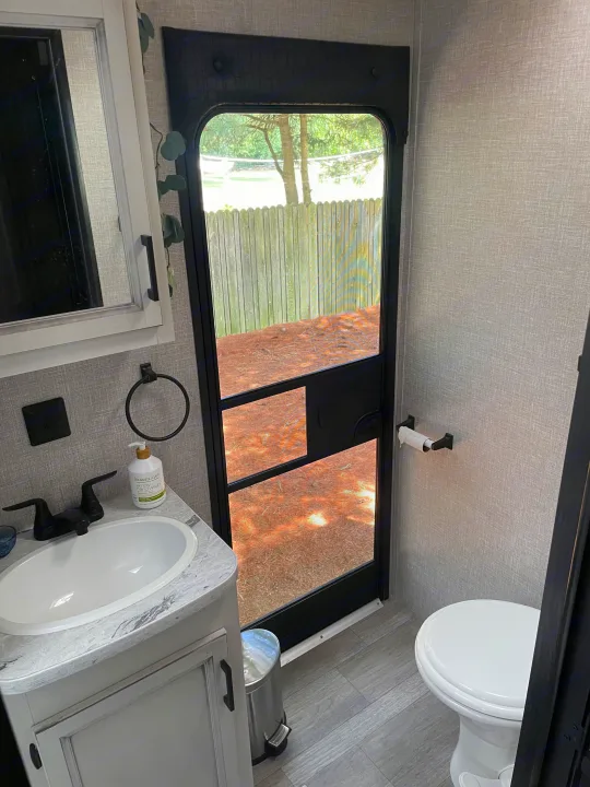 RV rental bathroom: modern sink, toilet, and clear screen door view of fenced yard with trees.. Jayco Jay Flight 2022