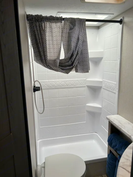 Clean RV rental bathroom featuring a white shower stall with curtain, toilet, and towel storage.. Venture Stratus 2021