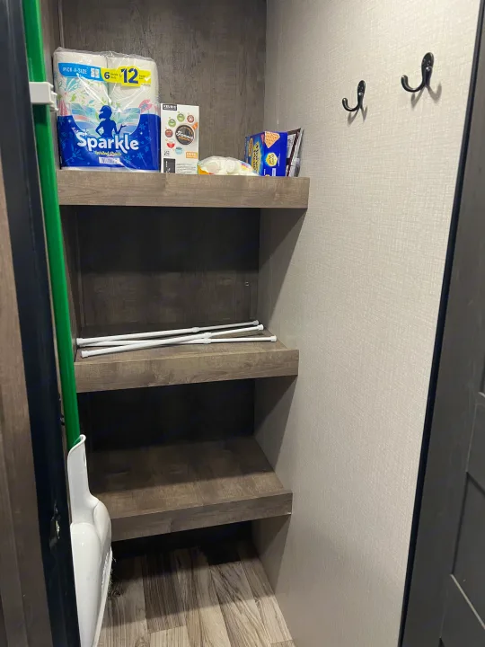 RV rental pantry: well-stocked shelves with paper towels, coffee pods, snacks, and a broom, plus hooks for organization.. Venture Stratus 2021
