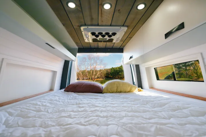 Cozy RV rental interior: white bed, pillows, modern cabinets, and a scenic lake view through the rear window.. Sovereign Vans Mercedes Benz Sprinter 2500 4*4 2024