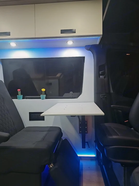 Detailed view of an RV rental's cozy interior, featuring plush seats, a retractable table, and blue LED accent lighting.. Sovereign Vans Mercedes Benz Sprinter 2500 4*4 2024