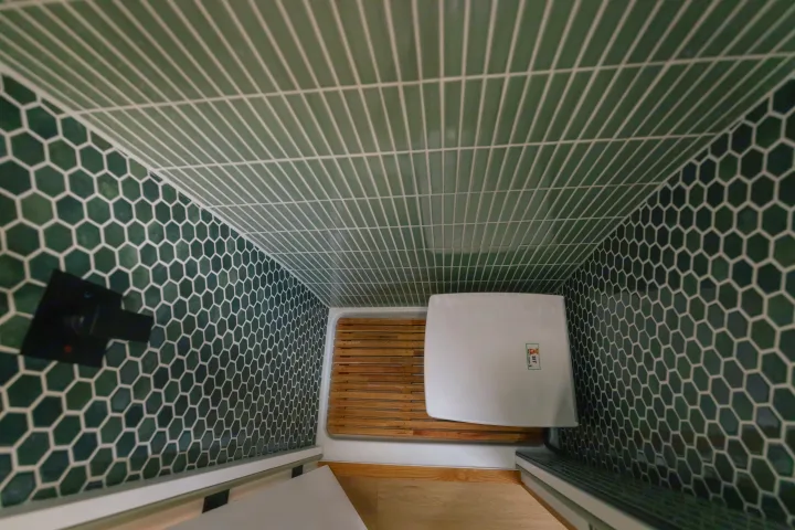 Inside an RV rental: a compact shower with green hexagonal & subway tiles, wooden mat, and a portable toilet.. Sovereign Vans Mercedes Benz Sprinter 2500 4*4 2024