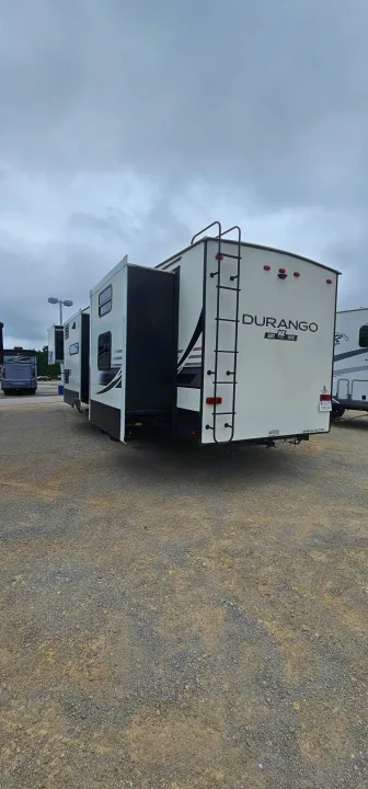 White Durango fifth-wheel RV with slide-outs deployed, parked on a gravel lot. Explore this spacious RV rental option.. K-Z Manufacturing Durango 2021