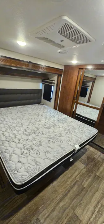 Clean RV rental bedroom with a large bed, decorative mattress, AC unit, and mirrored wardrobe for your travel comfort.. K-Z Manufacturing Durango 2021