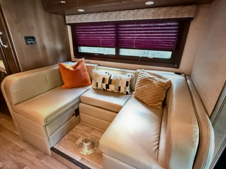 Inside a spacious RV rental: a comfortable cream dinette with accent pillows and purple window blinds.. Jayco Melbourne 2021