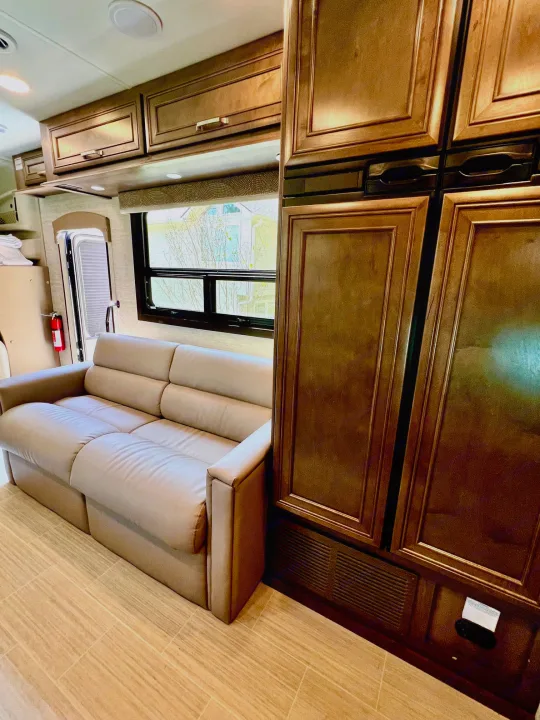 Spacious RV rental interior with a light sofa, dark wood cabinets, and large window. Perfect for your next trip.. Entegra Coach Esteem 2021