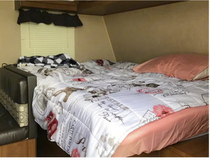 Cozy RV rental bedroom features a bed with Paris-themed comforter, pink pillow, and an adjacent bench.. Aspen Trail Aspen Trail Trailer 2017