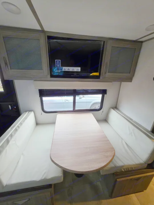 Inside an RV rental: a modern dinette with light wood table, plush benches, and an entertainment TV. Ideal for travel.. Keystone RV Passport SL Ultra Lite 2024