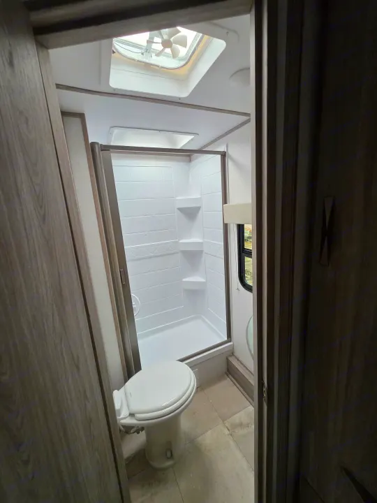 Inside an RV rental: a bright, compact bathroom featuring a shower, toilet, and ceiling fan for ventilation.. Keystone RV Passport SL Ultra Lite 2024