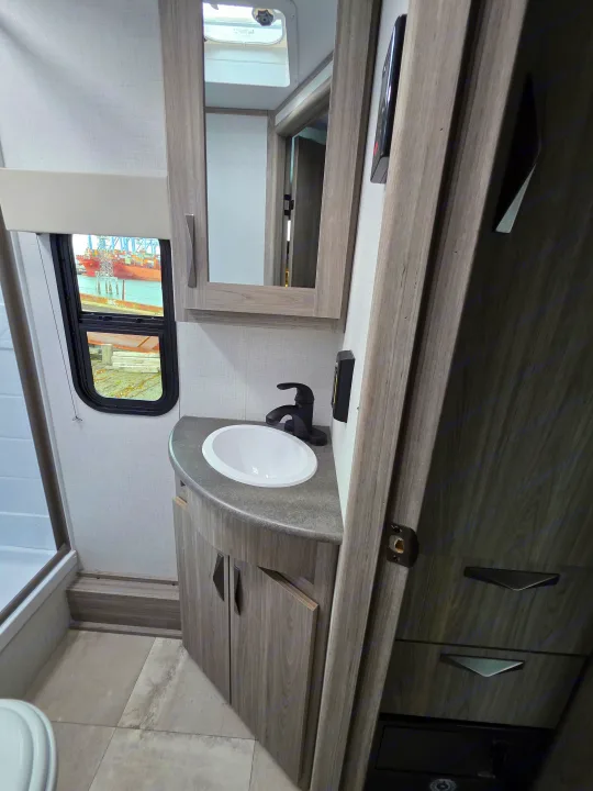 RV rental bathroom with modern sink, mirror, and window view of a ship. Part of shower visible on left.. Keystone RV Passport SL Ultra Lite 2024