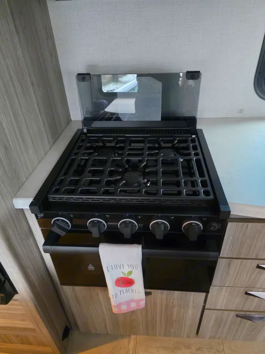 An RV rental kitchen features a compact stove and oven, complete with burners and control knobs, framed by light-toned cabinetry.. Keystone RV Passport SL Ultra Lite 2024