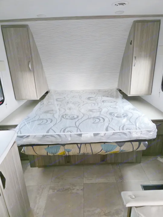 Spacious RV rental bedroom with a new mattress, overhead cabinets, and stylish patterned walls, ready for adventure.. Keystone RV Passport SL Ultra Lite 2024