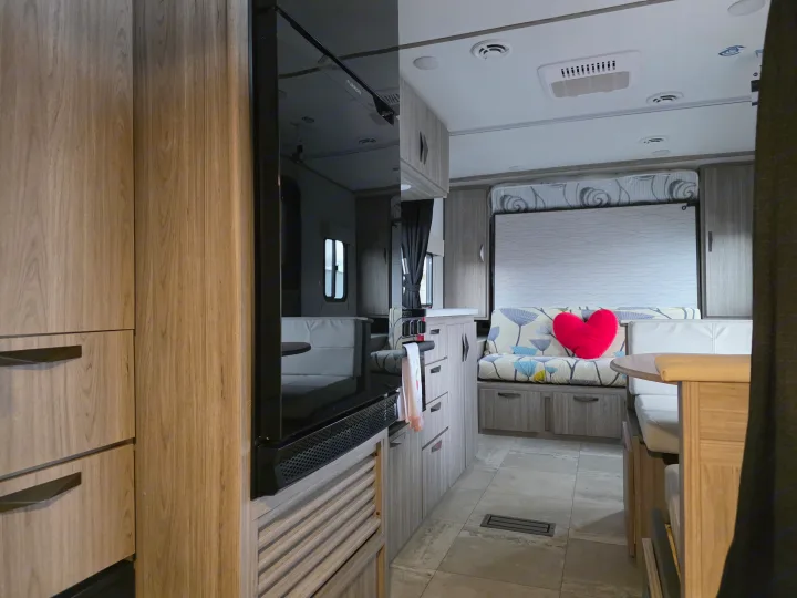 RV rental interior: Kitchen with fridge, dining area, and sleeping space, featuring a red heart pillow.. Keystone RV Passport SL Ultra Lite 2024