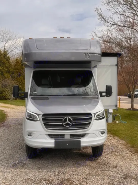Front view of a white & grey Winnebago motorhome, perfect for rv rental, parked on gravel with awning extended.. Winnebago View 2022