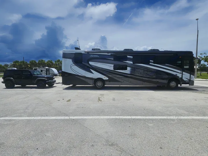 A large Berkshire XL RV, dark grey and white, tows a black Jeep. This setup is perfect for exploring, consider an RV rental.. Berkshire XL 2022