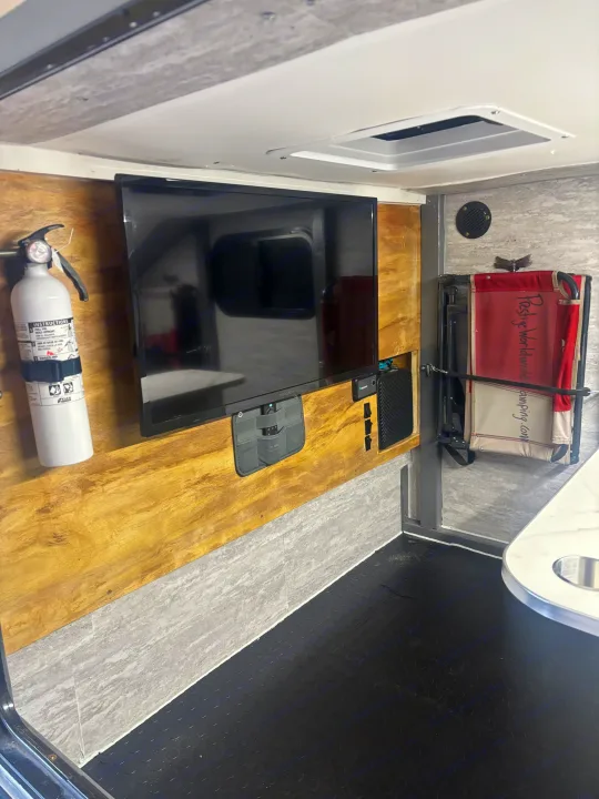 Interior of an RV rental: TV, fire extinguisher, power station, and foldable chair for comfortable travel.. Overlander HMDE 2025