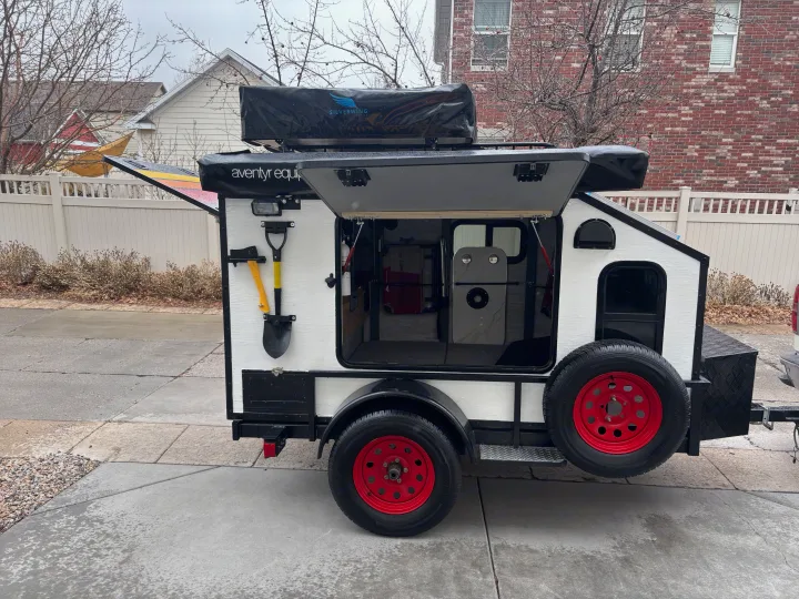 This compact white and black adventure trailer, featuring a rooftop tent and gear storage, is perfect for your next RV rental.. Overlander HMDE 2025