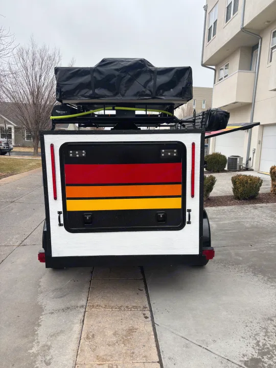 Rear view of an RV rental camper with a black rooftop tent & colorful stripes, prepped for adventure.. Overlander HMDE 2025