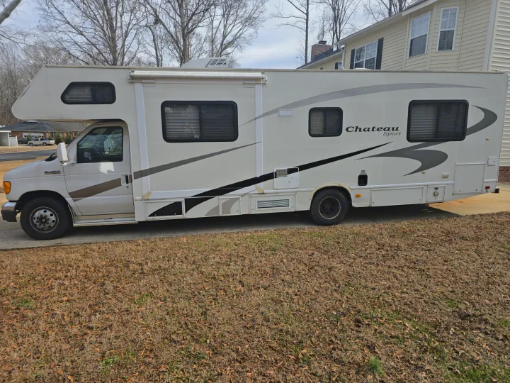 A white Chateau Sport RV rental, a large motorhome, is parked on a driveway with dry grass beside it.. Four Winds Chateau Sport 2006
