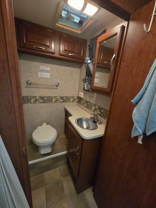 Inside an RV rental bathroom, featuring a compact toilet, sink, and overhead cabinets with specific waste instructions.. Four Winds Chateau Sport 2006