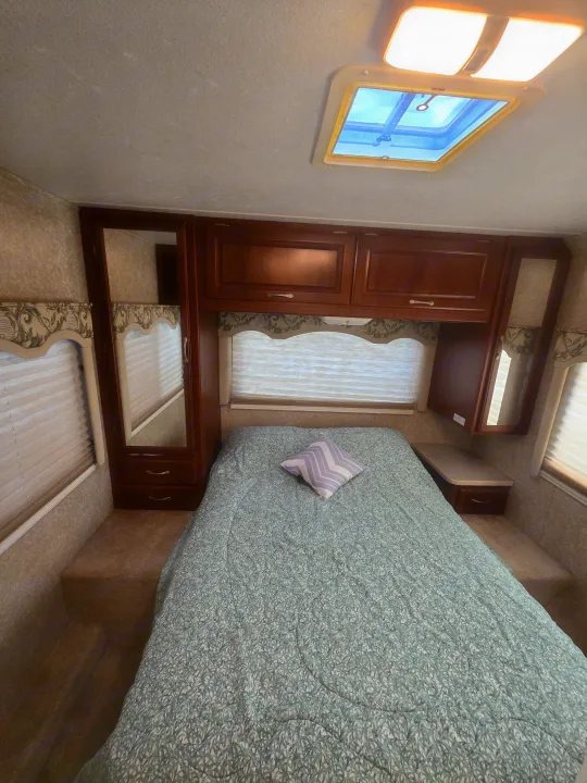 Cozy RV rental bedroom featuring a patterned comforter, mirrored closet, overhead storage, and skylight.. Four Winds Chateau Sport 2006