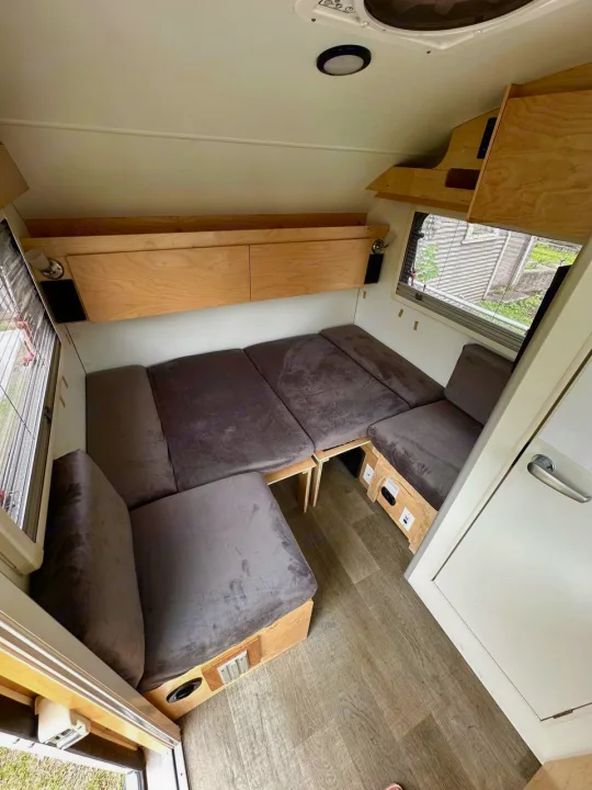 Cozy RV rental interior features a versatile convertible bed, ample overhead storage, and wood-look flooring.. nuCamp T@B 2022