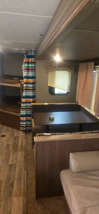 RV rental interior: bunk beds with a striped curtain, dinette table, and wood-look flooring.. Keystone RV Hideout LHS 2018
