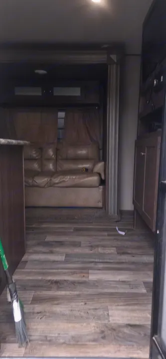 View inside an RV rental showing a living area with a tan sofa, entertainment center, and wood-look floor.. Keystone RV Hideout LHS 2018