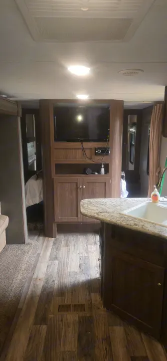 Inside an RV rental: a living space with an entertainment center, kitchen island with sink, and wood-look flooring.. Keystone RV Hideout LHS 2018