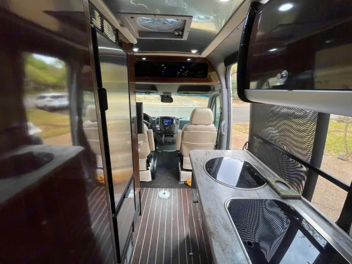 RV rental: Interior view of a modern camper van showing its kitchen, wood floor, and front cabin with swivel seats.. Airstream Interstate 2018