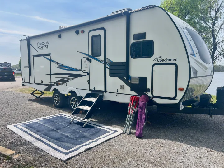 This white Coachmen Freedom Express RV rental is set up by a lake with an outdoor mat & chairs, ready for camping.. Coachmen Freedom Express 2020