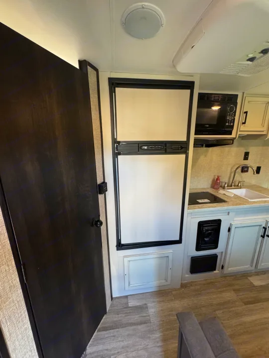 RV rental kitchen and living area showcasing a fridge, microwave, sink, cabinets, and a dark wood door.. Jayco Jay Flight SLX 2022