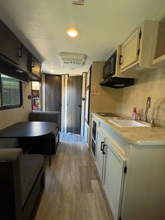 Spacious modern RV rental interior showing a light-toned kitchen with sink & microwave, and dark-padded dinette.. Jayco Jay Flight SLX 2022